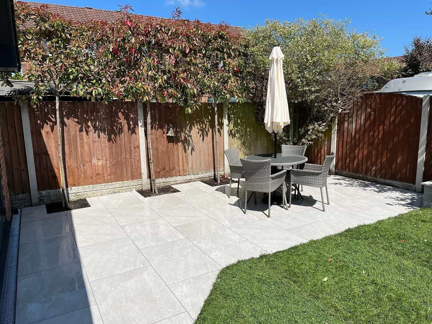 Patio installation featuring Rasa White Matte 24x36x2cm Rectified Porcelain Pavers by STONELUX. The elegant white tiles create a modern outdoor space, complemented by wicker furniture and lush greenery, ideal for a stylish hardscape project.