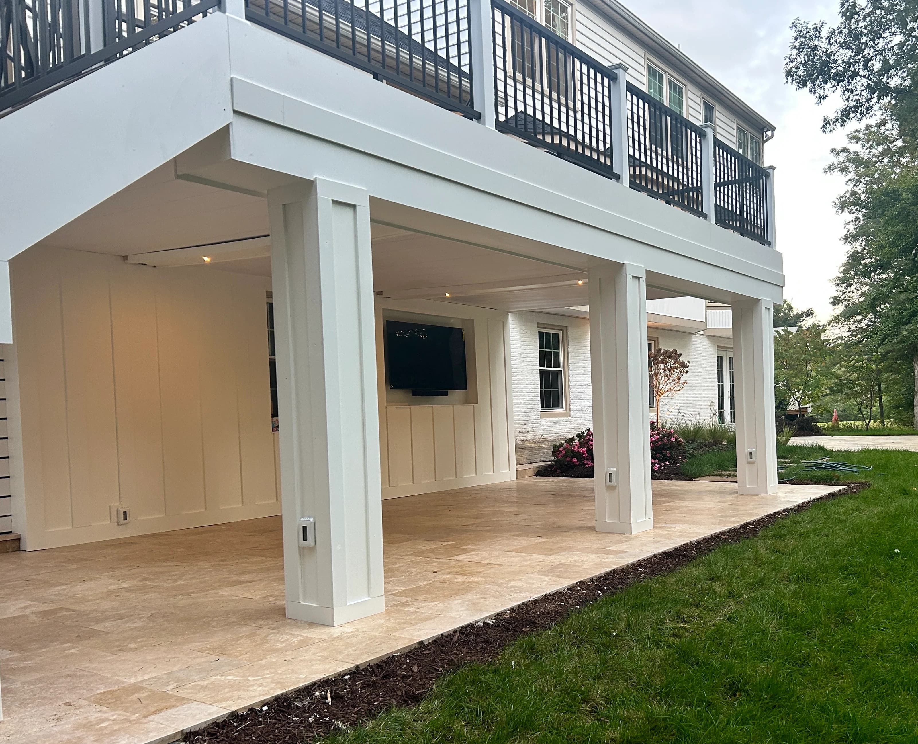 Ivory Travertine Tumbled French Pattern 3cm Paver installed on a modern patio. The natural stone's beige tones complement the white facade and black railing. Surrounded by lush greenery and classic architecture, ideal for pool decks and outdoor living ...