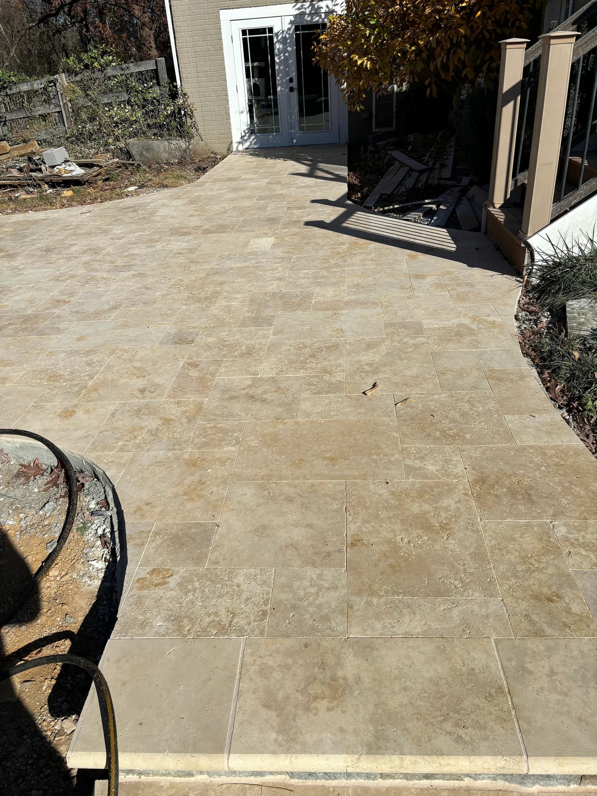 Ivory Travertine Tumbled French Pattern 3cm Paver installed on a patio. The natural stone's warm beige tones and tumbled finish create a classic look. Surrounded by a garden and modern architecture, perfect for hardscape projects and outdoor renovations.