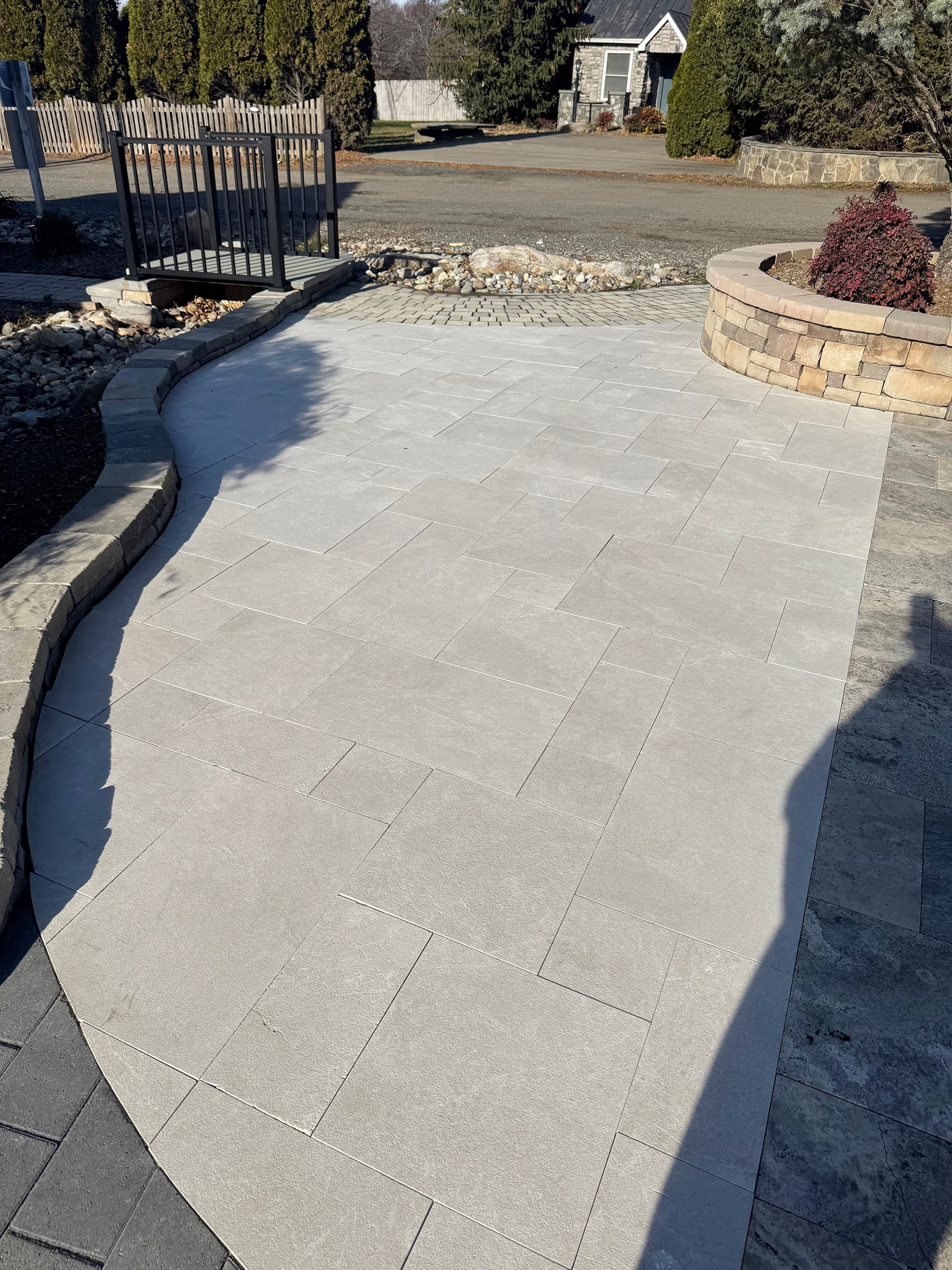Pera Cream Marble Sand Blasted French Pattern 3cm Paver installation on a patio. The light cream marble complements the rustic stone wall and landscaping. Ideal for outdoor spaces, enhancing elegance with natural stone texture and contemporary design.
