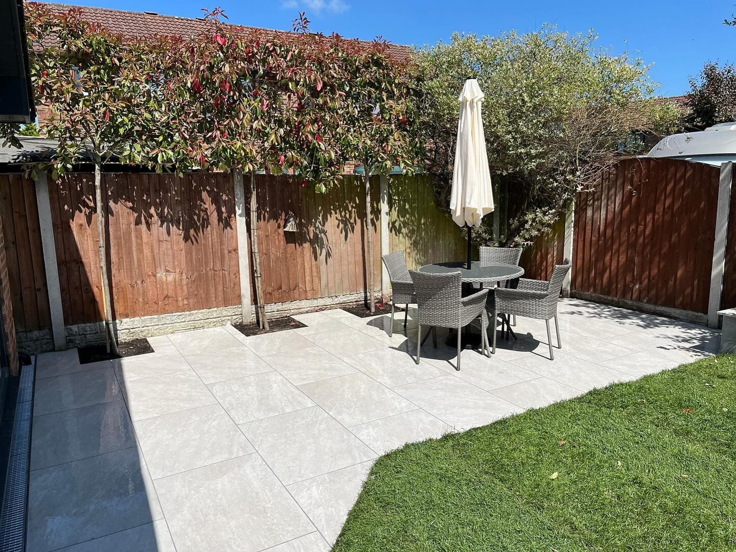 Patio installation featuring Rasa White Matte 24x36x2cm Rectified Porcelain Pavers by STONELUX. The elegant white tiles create a modern outdoor space, complemented by wicker furniture and lush greenery, ideal for a stylish hardscape project.