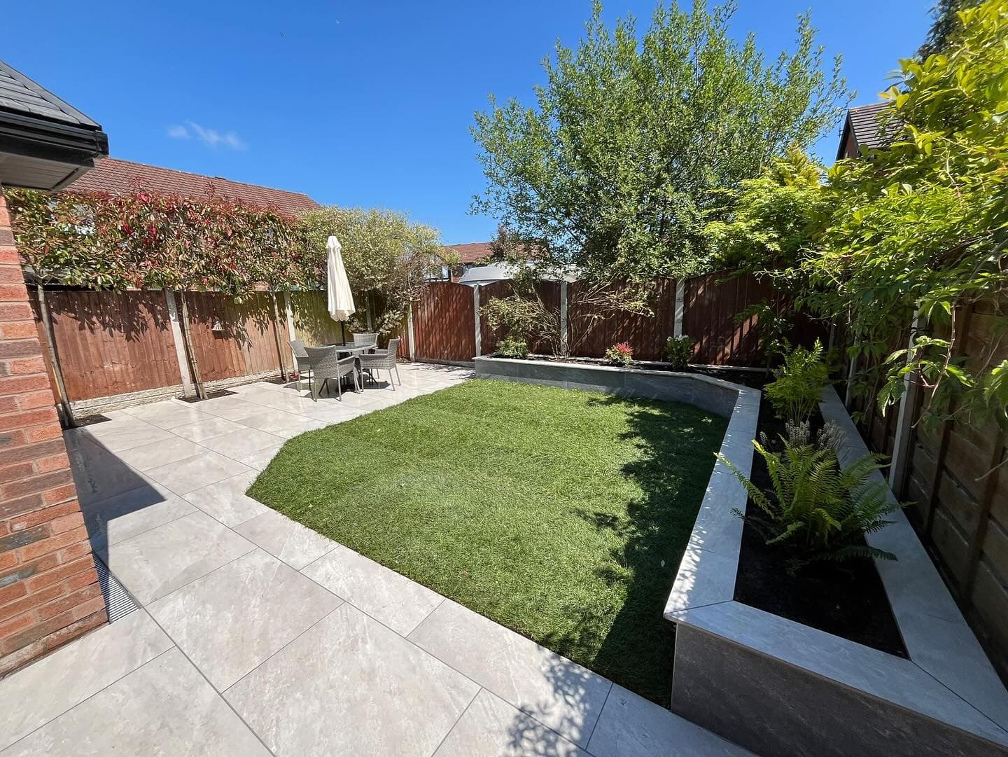 Outdoor patio featuring Rasa White Matte 24x36x2cm Rectified Porcelain Pavers. The light-toned pavers create a modern, seamless look, complementing lush greenery and a stylish outdoor dining set. Ideal for hardscape projects and contemporary designs.