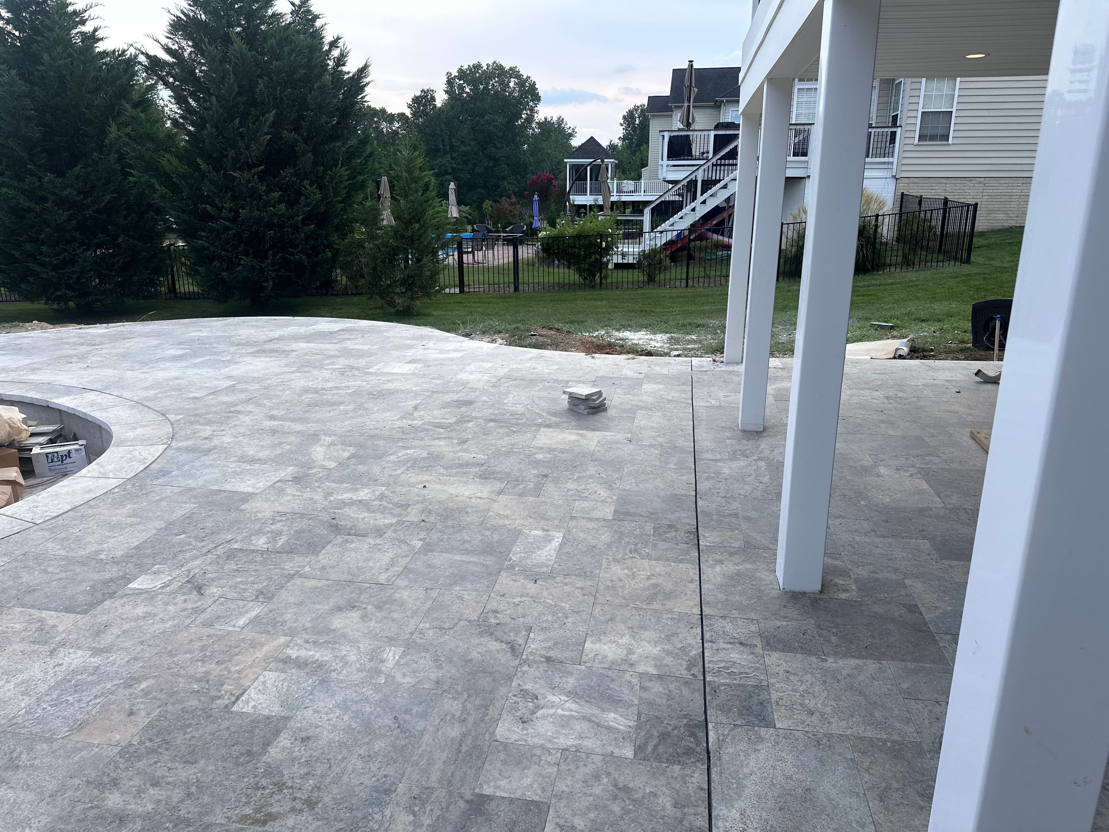 Silver Travertine Tumbled French Pattern 3cm Paver - Premium used in a patio installation. The natural stone pavers create a classic look with their soft gray tones and subtle veining. Surrounded by lush greenery and adjacent to a modern home, this har...