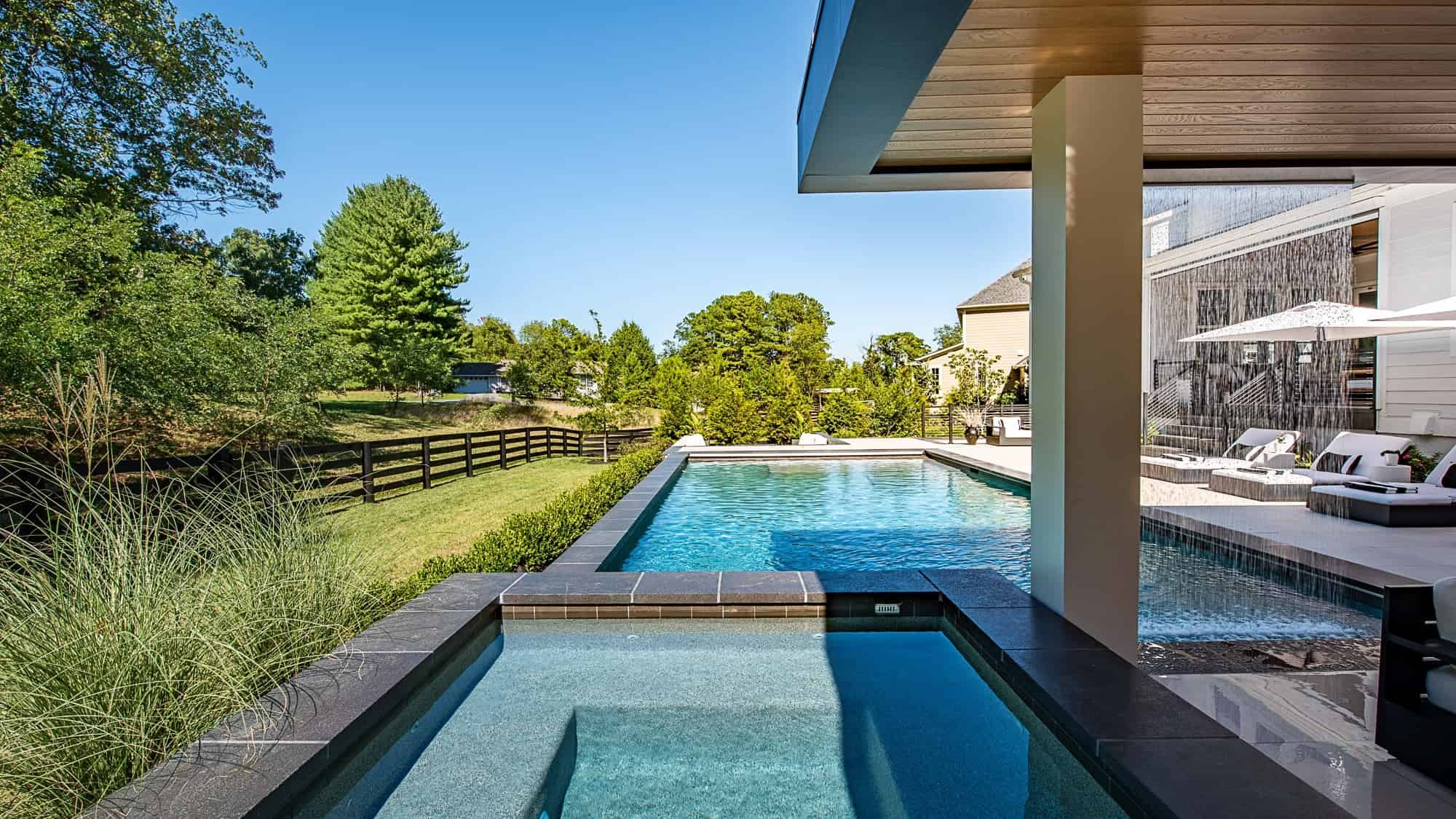 Modern Aldie pool and patio with Black Basalt coping, porcelain pavers, raised spa, and covered outdoor living area.