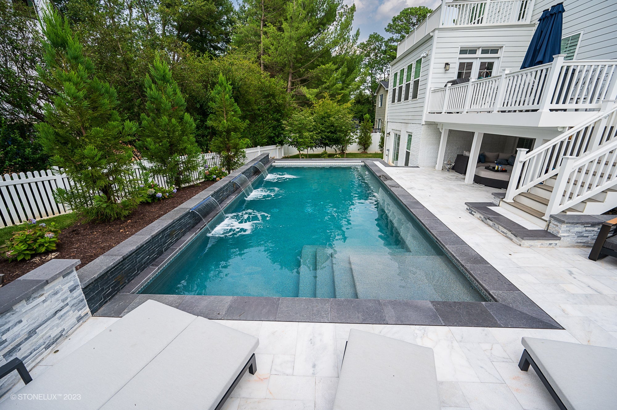 Luxurious pool installation featuring Afyon White Marble pavers by STONELUX. Elegant pool deck with marble and dark stone coping, surrounded by lush greenery and modern architecture, creating a serene outdoor retreat. Perfect for pool renovations and h...