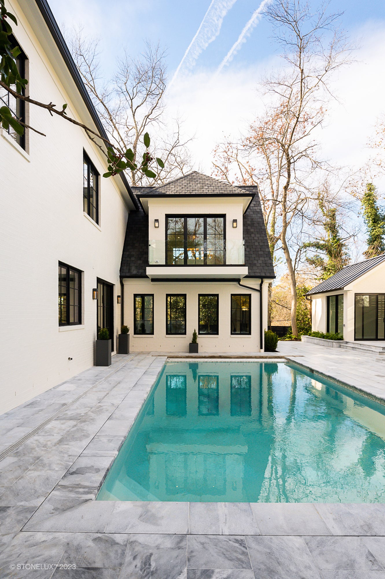 Luxurious outdoor pool area featuring Arctic Grey Marble by STONELUX. The natural stone pavers surround the pool, complementing the modern architecture with sleek lines and a serene blue pool. Ideal for upscale hardscape and pool renovation projects.