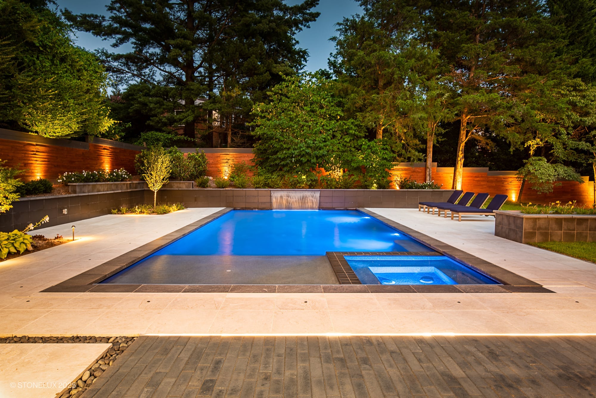Luxurious modern pool installation featuring Stonelux Black Basalt natural stone as pool coping, surrounded by elegant porcelain pavers. The serene blue pool water complements lush landscaping and stylish outdoor furniture, creating a tranquil oasis.