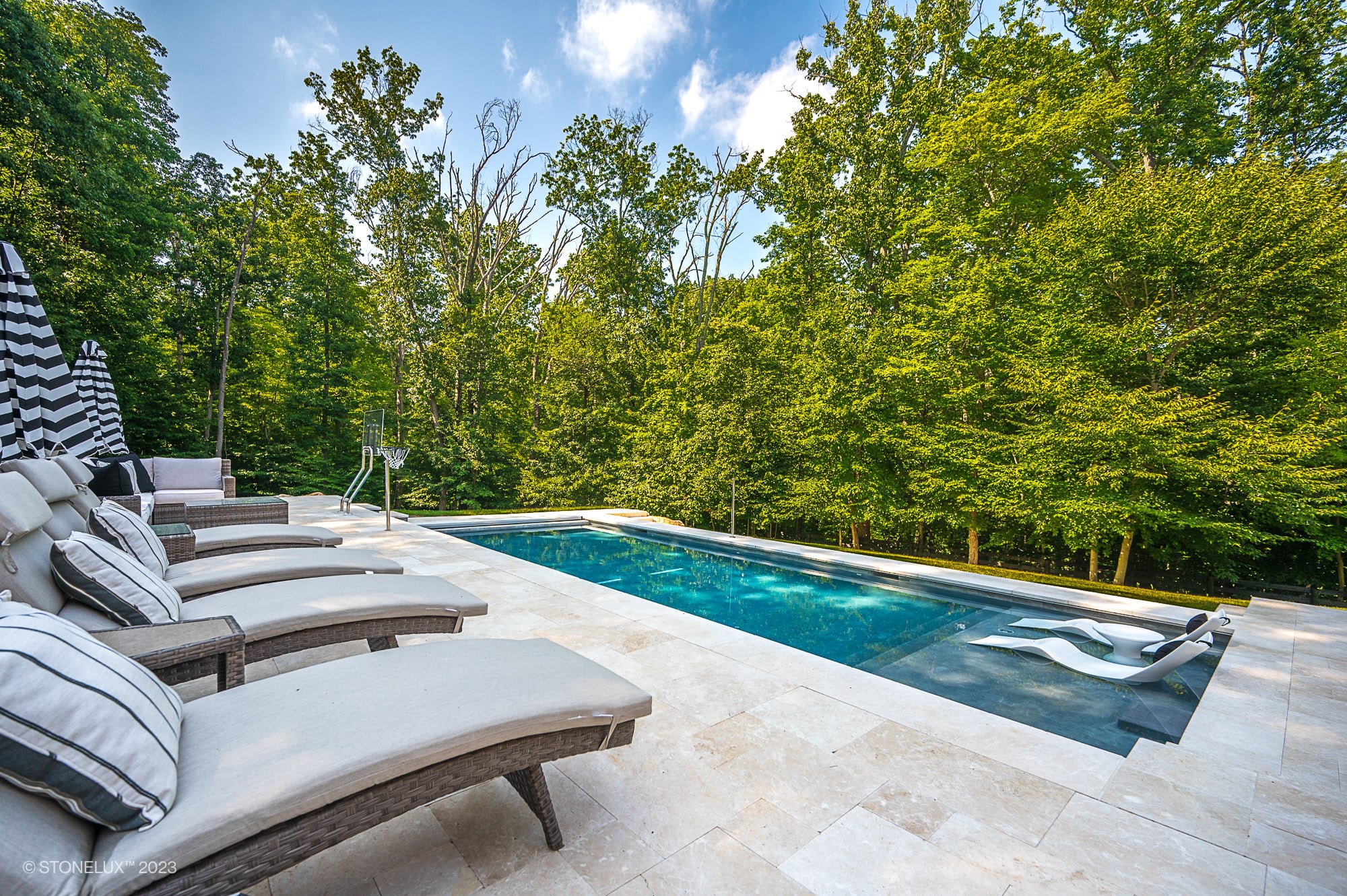 Luxurious poolside setting featuring Pera Cream Marble pavers by STONELUX. The elegant marble surrounds a sparkling blue pool, complemented by chic lounge chairs and lush greenery. Ideal for modern outdoor living and hardscape projects.