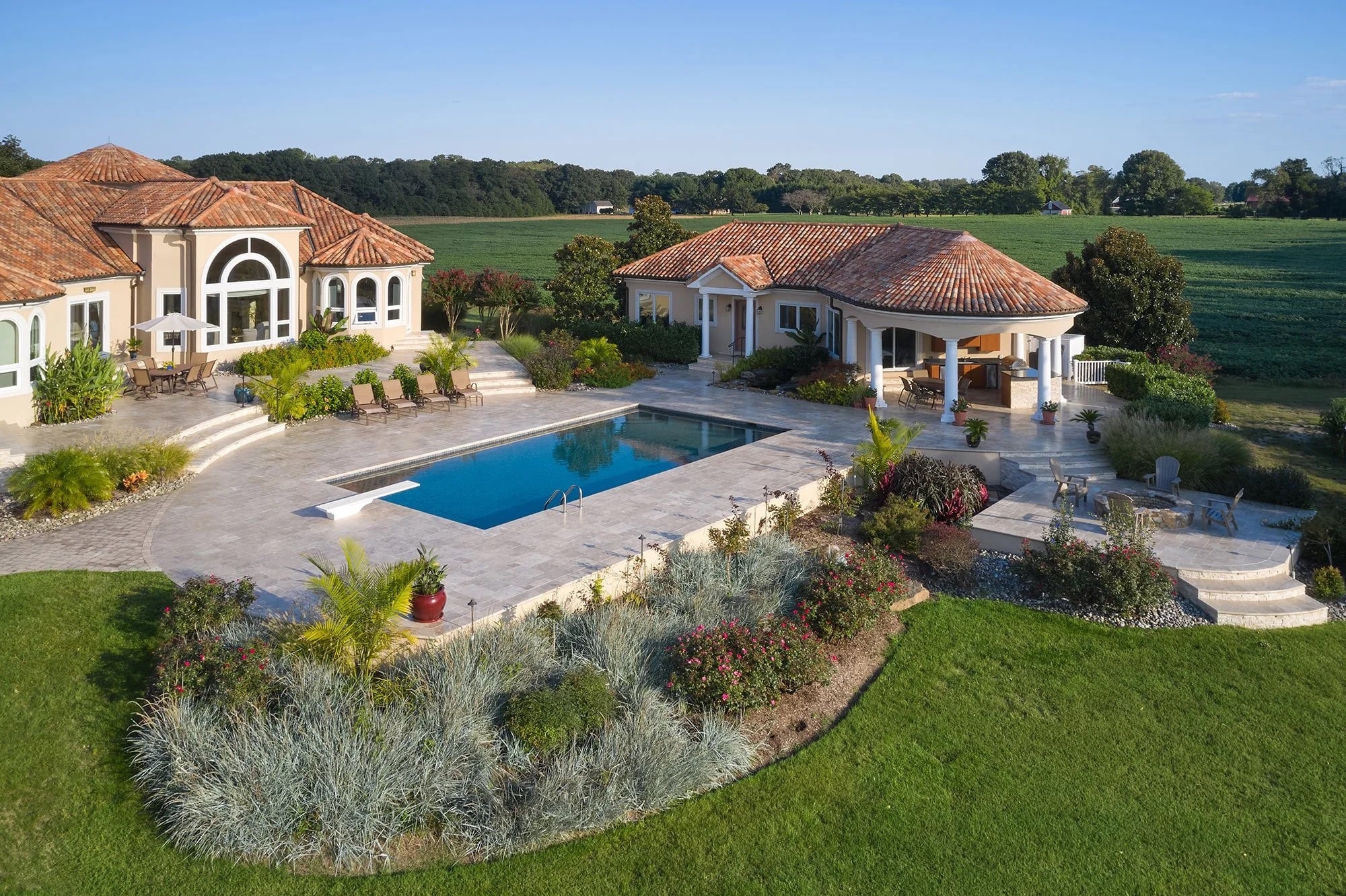 Luxurious poolside retreat featuring Philly Travertine natural stone patio and pool deck. The elegant design complements Mediterranean-style architecture, lush landscaping, and a sparkling blue pool, creating a stunning outdoor oasis ideal for relaxation.