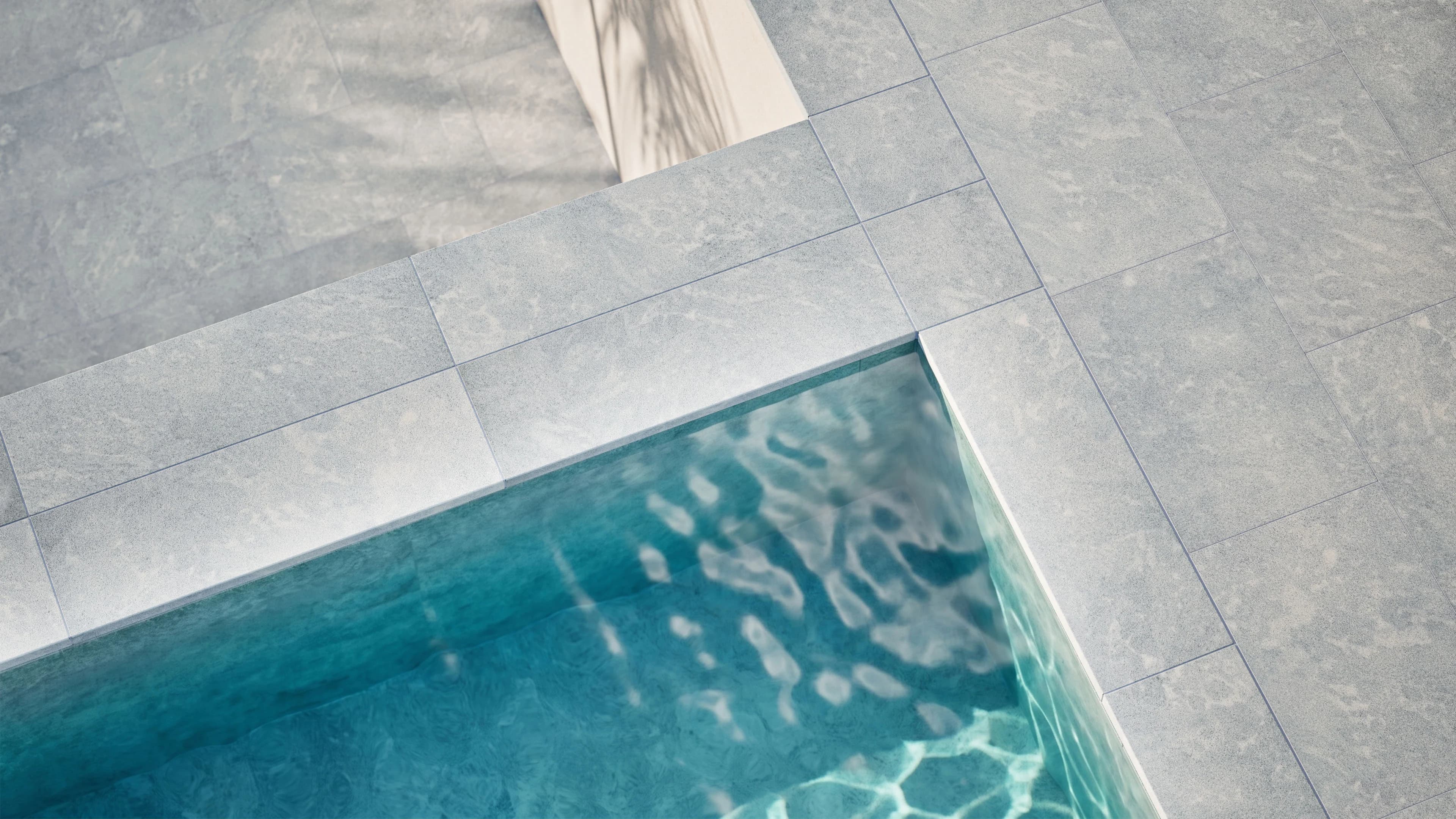 Afyon Grey Marble Sand Blasted 16x48x2 Single Bullnose Coping installed around a modern pool. The marble's subtle grey tones and sandblasted finish complement the clear blue water, creating a sleek, contemporary outdoor space. Ideal for luxury hardscap...