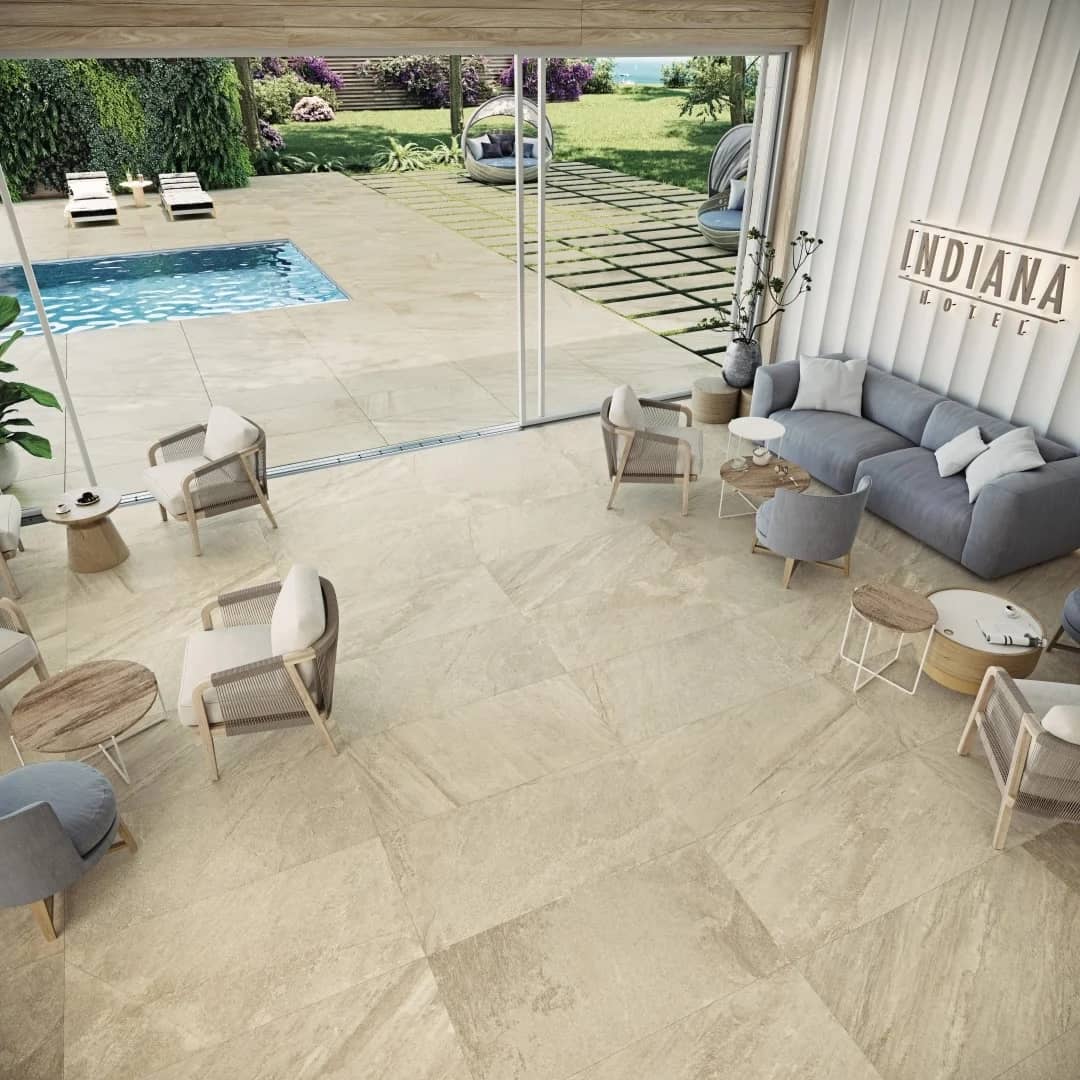 Indiana Beige Matte 24x48x2cm Rectified Porcelain Paver installed in a modern outdoor patio and pool area. The matte porcelain finish complements the luxurious seating, lush greenery, and serene blue pool, enhancing the elegant hardscape design.