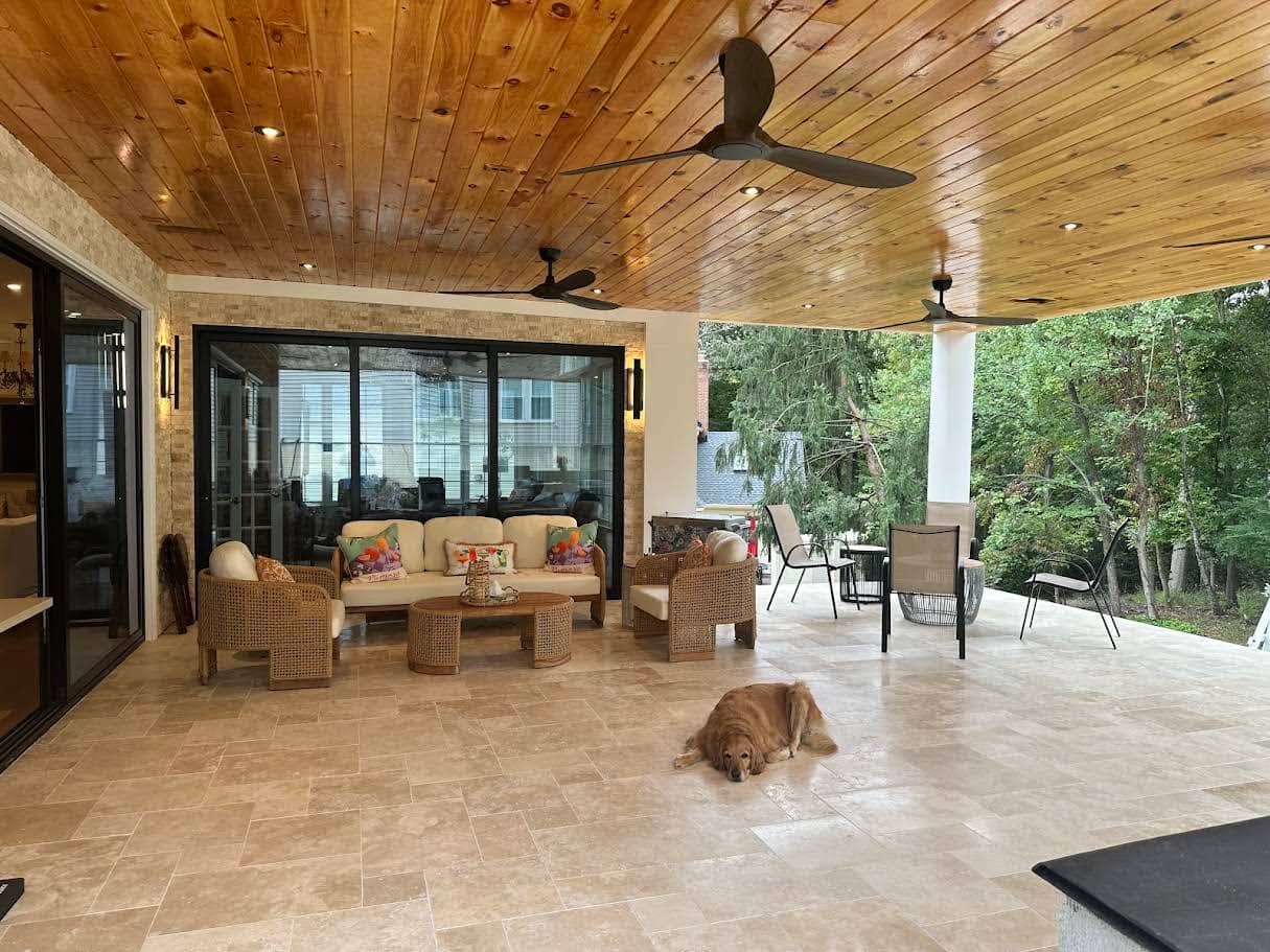 Ivory Travertine Tumbled French Pattern 3cm Paver used in a luxurious patio setting. The travertine's warm, creamy tones complement the rustic wooden ceiling and wicker furniture. The spacious outdoor area is surrounded by greenery, creating a serene a...