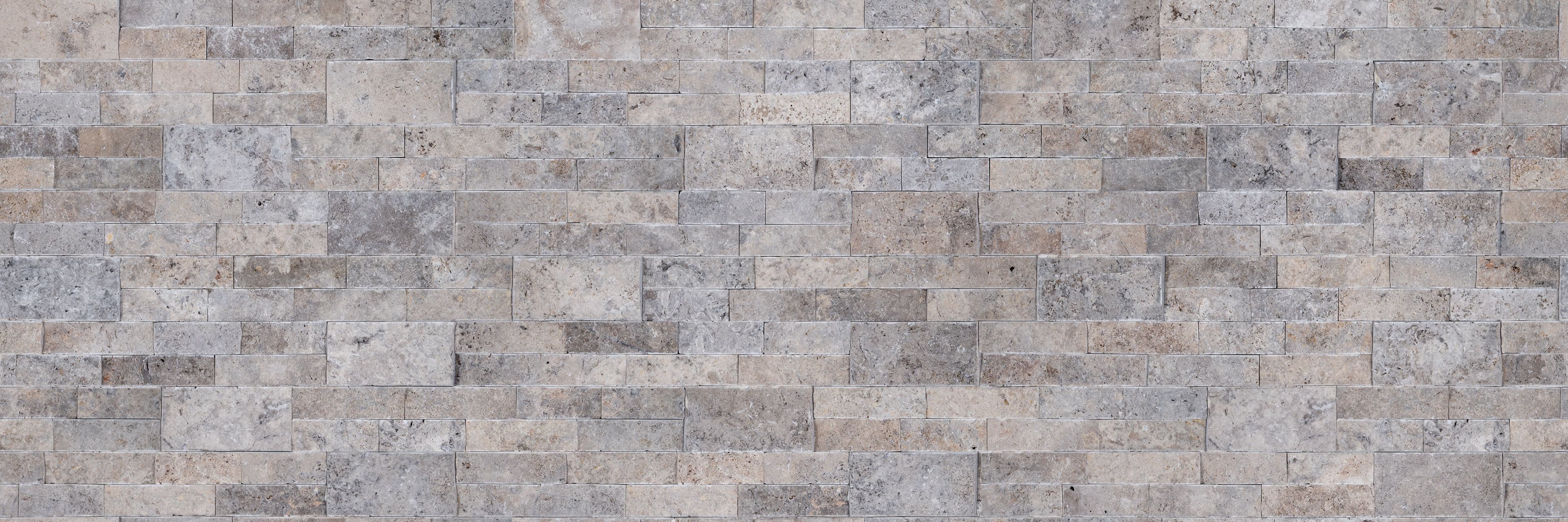 Close-up of Silver Travertine Splitface Ledger Panel by STONELUX, showcasing a 6x24 veneer with a textured splitface finish. Features a mix of gray and beige tones with natural veining, ideal for wall applications in hardscape projects.