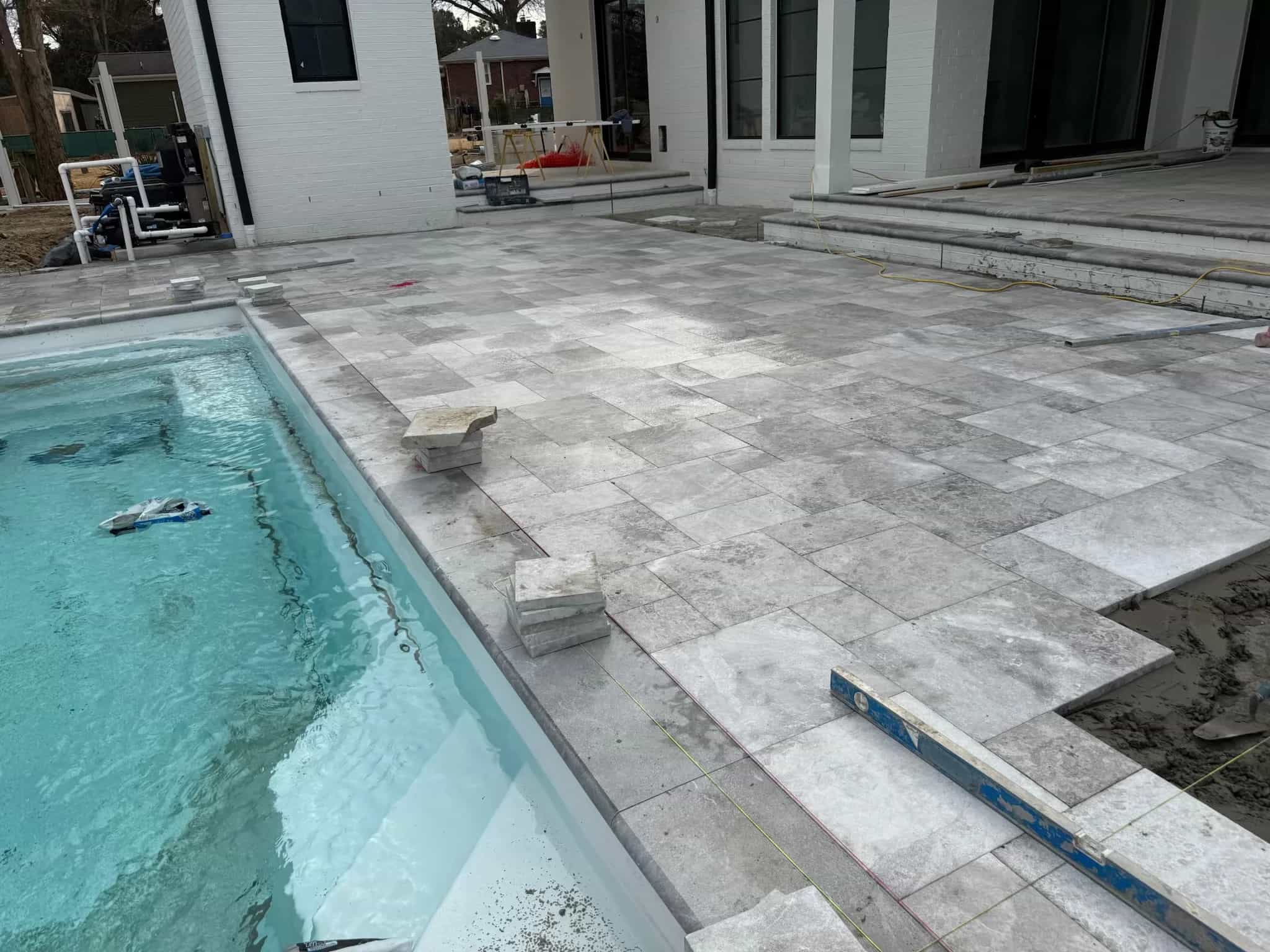 Installation of Tundra Grey Marble Sand Blasted French Pattern 3cm Pavers around a modern pool. The marble's grey tones and subtle veining complement the clear blue water and white architecture, creating a sleek, luxurious outdoor space.