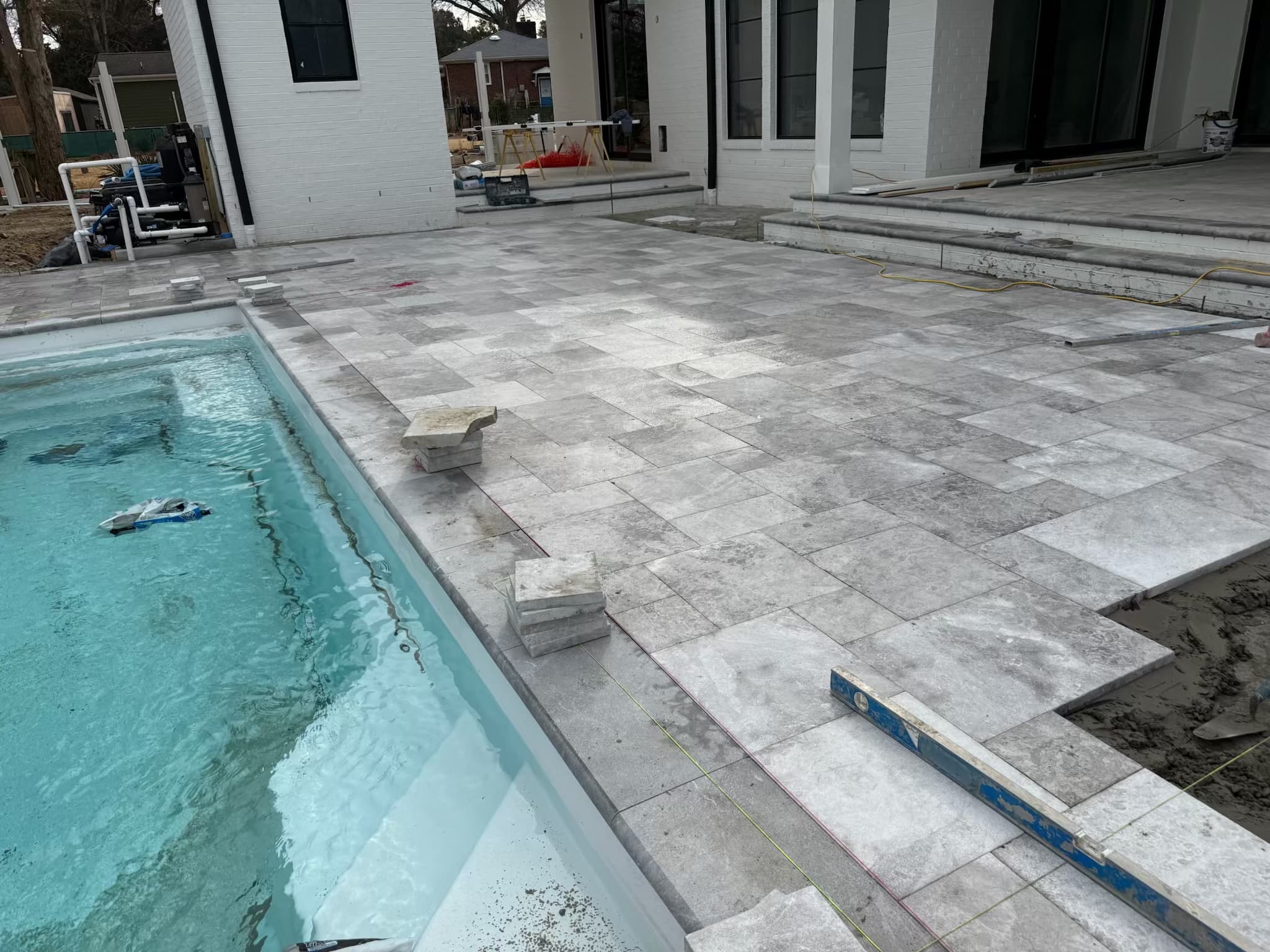 Installation of Tundra Grey Marble Sand Blasted French Pattern 3cm Pavers around a modern pool. The marble's grey tones and subtle veining complement the clear blue water and white architecture, creating a sleek, luxurious outdoor space.