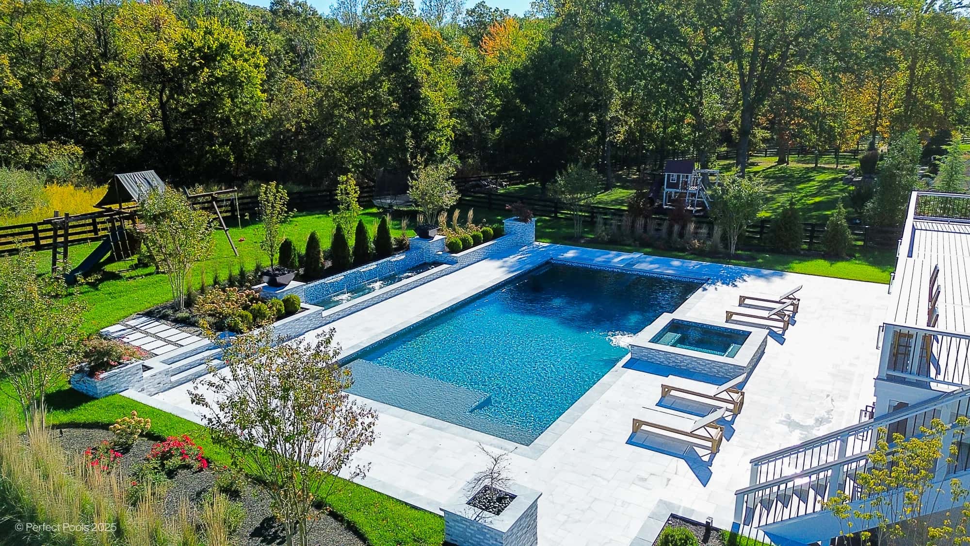 Aldie Serenity project in Aldie, VA features Afyon White and Arctic Grey marble surrounding a luxury pool. The modern design includes matching pavers, blue water, and wooden lounge chairs, set against lush landscaping and a sunlit backyard ambiance.