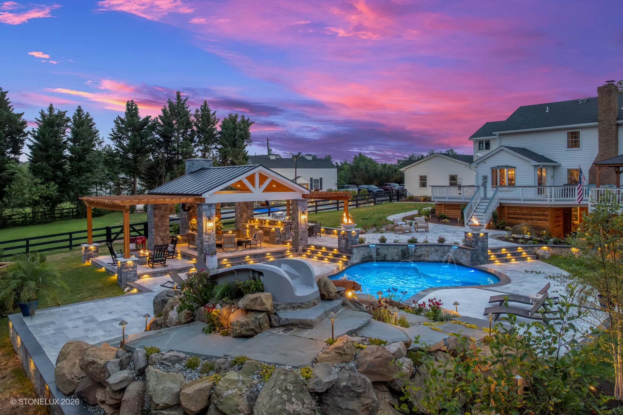 Backyard oasis in McLean, VA featuring Tundra Grey Marble and Black Basalt from Stonelux. Modern design with Afyon White Marble accents, blue pool, lush landscaping, wooden pergola, and ambient lighting. Ideal for luxury pool and hardscape projects.