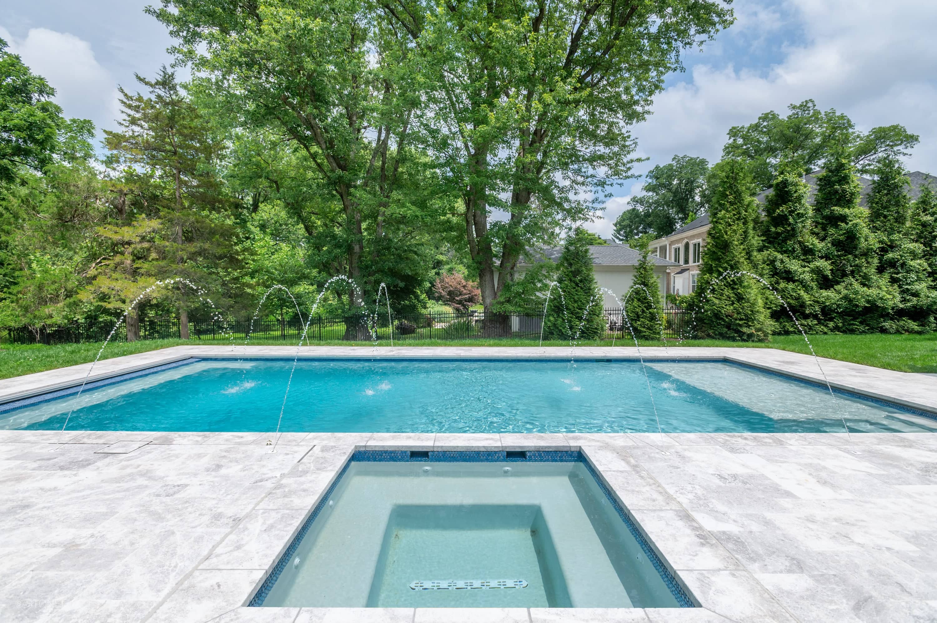 Modern pool retreat in McLean with Tundra Grey Harmony marble from STONELUX. The sleek design features elegant pavers complementing the blue pool water, surrounded by lush greenery and a stylish residential backdrop, exuding tranquility.