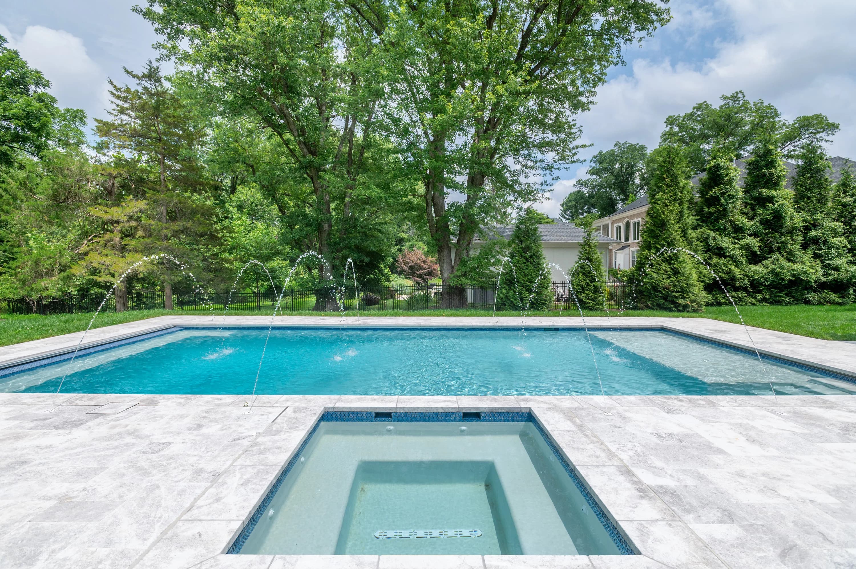 Modern pool retreat in McLean with Tundra Grey Harmony marble from STONELUX. The sleek design features elegant pavers complementing the blue pool water, surrounded by lush greenery and a stylish residential backdrop, exuding tranquility.