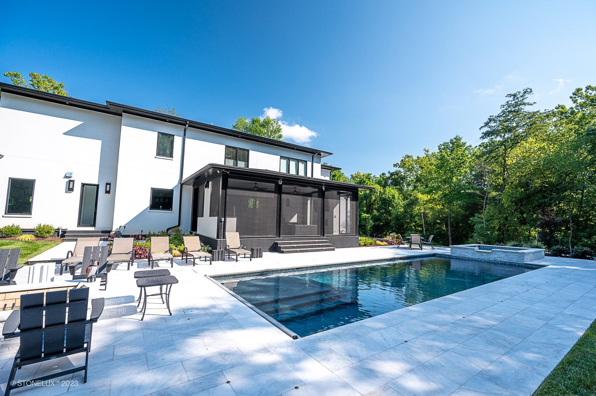 Afyon Elegance: Modern White Marvel with Black Accents poolside, this stunning house boasts a white exterior, large windows, a screened-in porch, marble patio, and in-ground pool—surrounded by trees and blue sky with stylish outdoor seating.