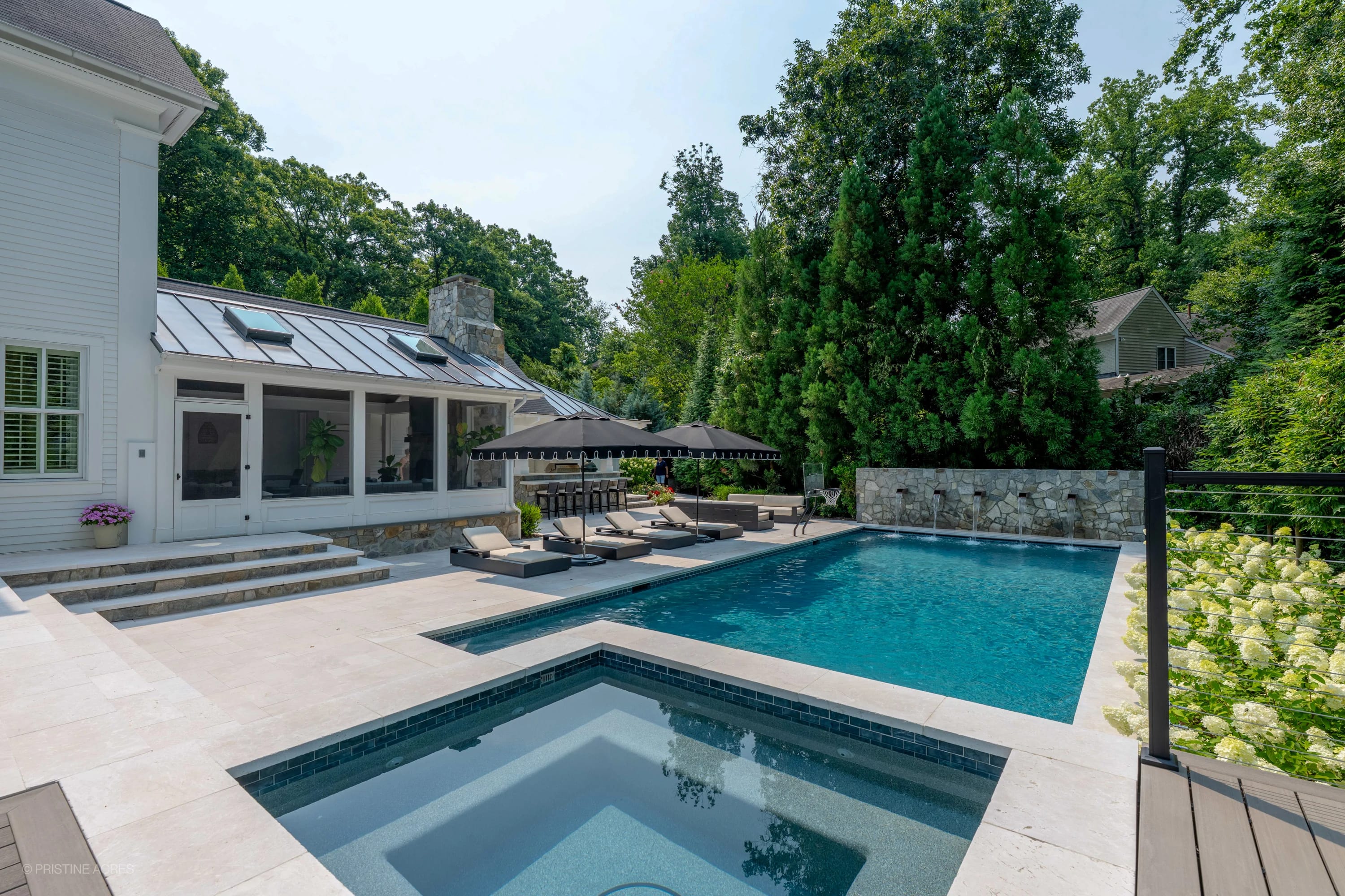 Luxurious Pera Cream Marble pool and patio in McLean, VA. Featuring elegant marble pavers, modern outdoor furniture, vibrant blue pool water, and lush greenery. Stone wall complements white architecture, creating a serene, upscale outdoor living space.