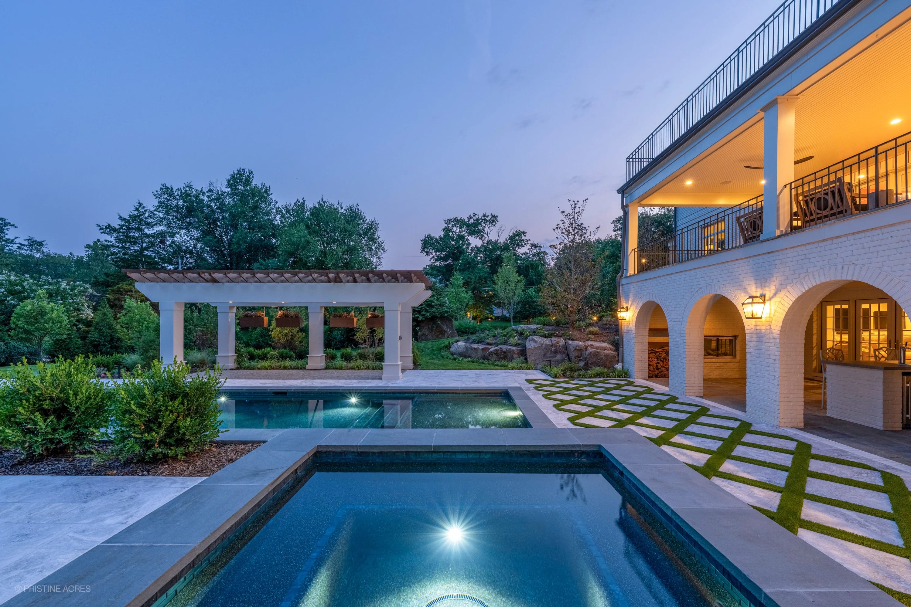 Luxurious Tundra Grey Marble pool deck with Bluestone coping in McLean, VA. Features a serene blue pool, elegant pergola, lush landscaping, and modern architecture. Evening lighting enhances the contemporary backyard retreat ambiance.